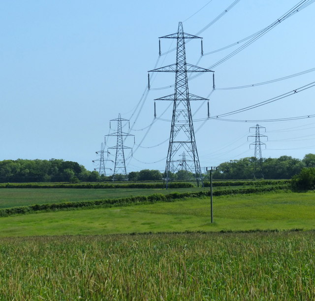 Steel electricity pylons supporting overhead transmission lines across green fields near Grafham Water in Cambridgeshire.